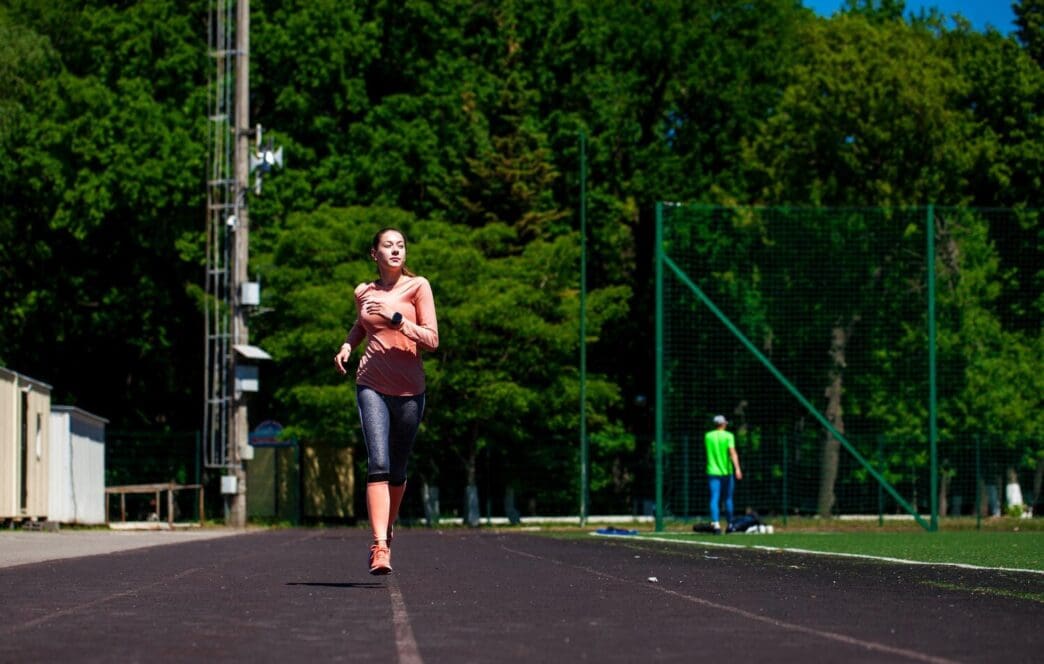 A young, beautiful woman runs on a track in a stadium.