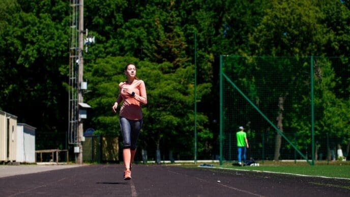 A young, beautiful woman runs on a track in a stadium.