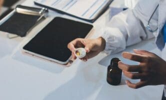 A young brunette woman sits at a doctor's desk during a consultation.