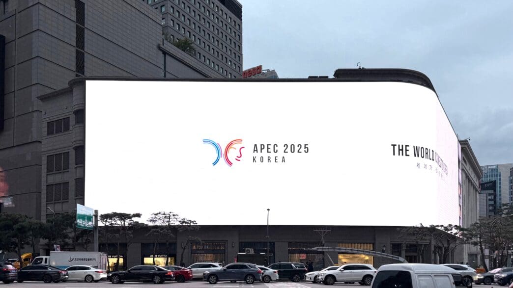 Large LED screen on a building displaying the APEC 2025 Korea logo in a city square.