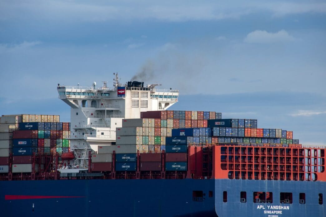 The superstructure and fully loaded decks of the massive container ship APL Yangshan sailing on a calm strait under a cloudy sky