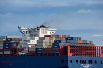 The superstructure and fully loaded decks of the massive container ship APL Yangshan sailing on a calm strait under a cloudy sky