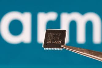 Tweezers hold a microchip displaying the STMicroelectronics and ARM logos against a blurred white "ARM" wordmark on a blue background.