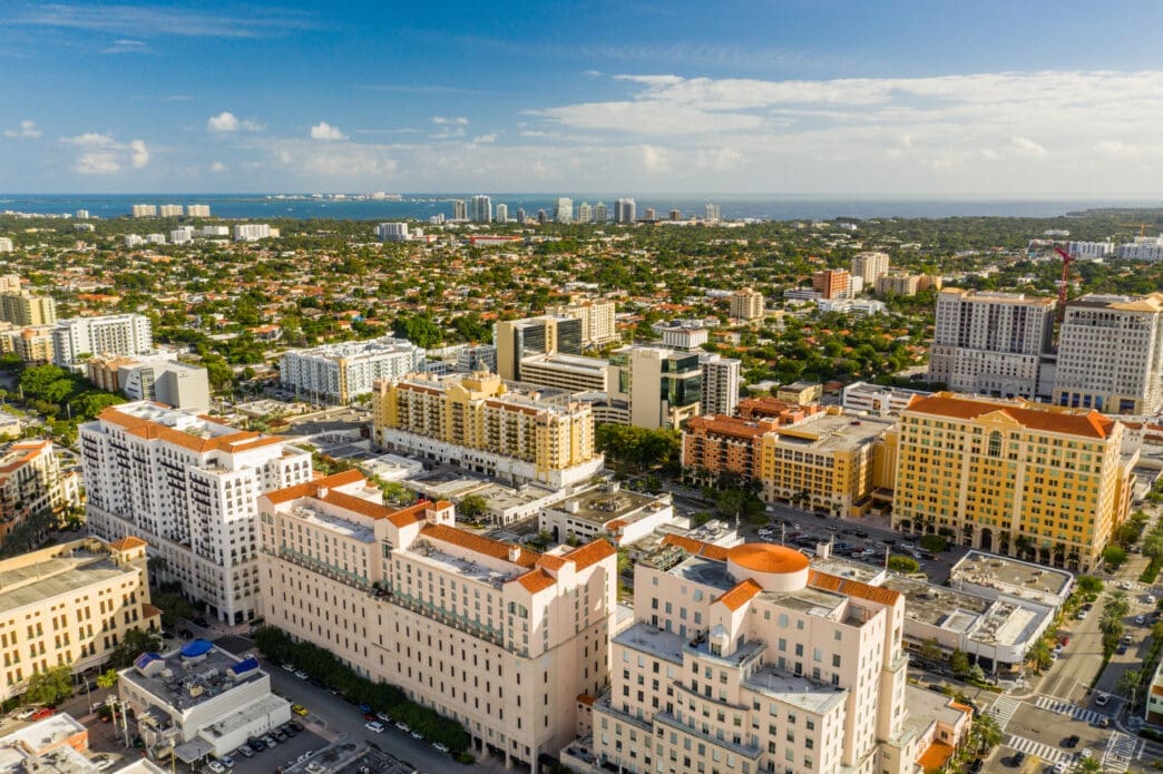 A beautiful aerial photo showing the dense city skyline of Coral Gables, Florida, under a blue sky.
