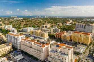 A beautiful aerial photo showing the dense city skyline of Coral Gables, Florida, under a blue sky.