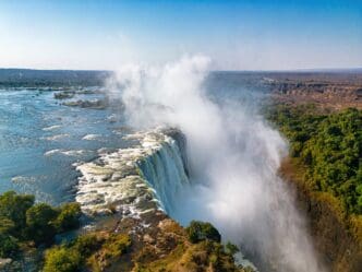 An aerial view of the powerful Victoria Falls on the Zambia-Zimbabwe border, with a huge plume of mist rising from the gorge.