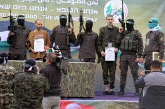Al-Qassam Brigades members with weapons and a certificate during a prisoner exchange event