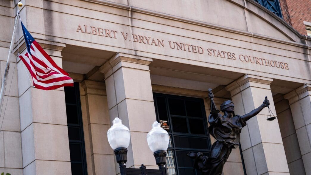 The stone facade of the Albert V Bryan United States Courthouse with a statue of Lady Justice and an American flag.