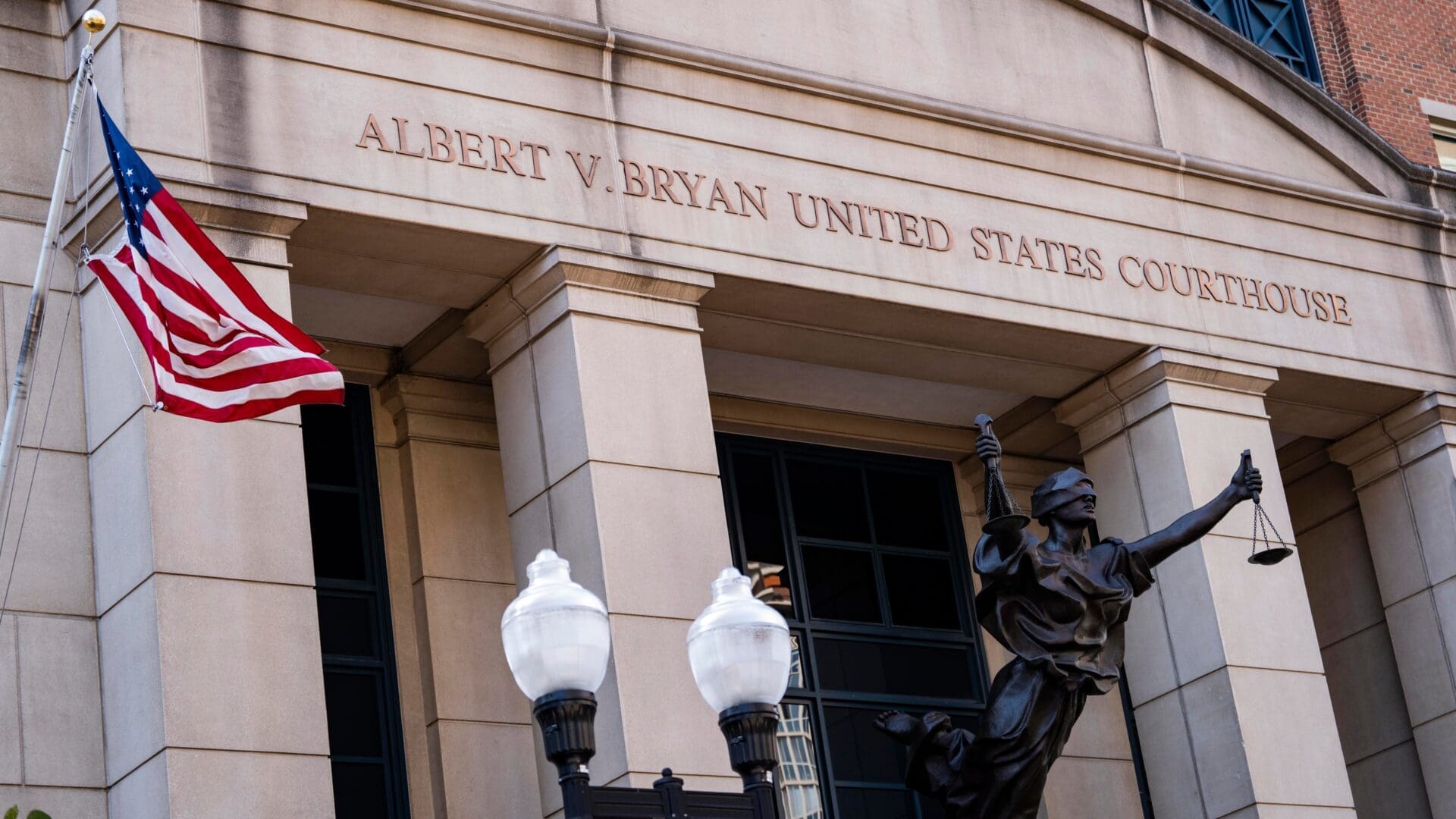 The stone facade of the Albert V Bryan United States Courthouse with a statue of Lady Justice and an American flag.