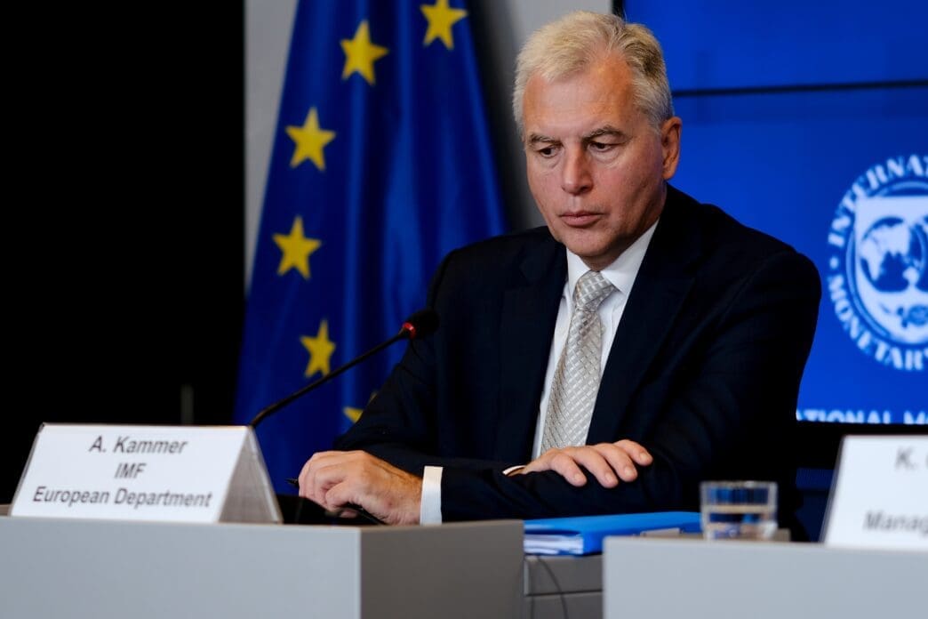 Alfred Kammer, IMF European Department Director, sits at a desk during a news conference with the EU and IMF logos in the background.