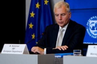 Alfred Kammer, IMF European Department Director, sits at a desk during a news conference with the EU and IMF logos in the background.