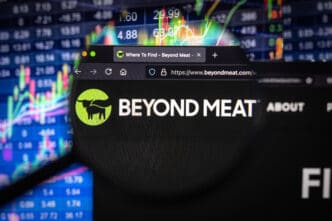 A magnifying glass focuses on the Beyond Meat logo and website URL on a computer screen, with a colorful stock chart in the background.