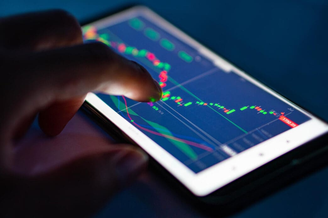 Finger interacting with a stock market chart on a smartphone screen.
