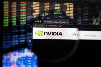A magnifying glass focuses on the Nvidia logo on its website, with a colorful, out-of-focus stock market chart in the background.