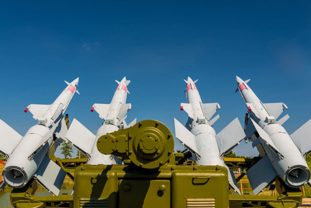 Four white surface-to-air missiles mounted on an olive green military launch vehicle against a clear blue sky.