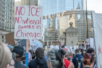 A protest sign reads "NO ICE NO national guards in Chicago!" held above a crowd, with the Trump Tower visible in the background.
