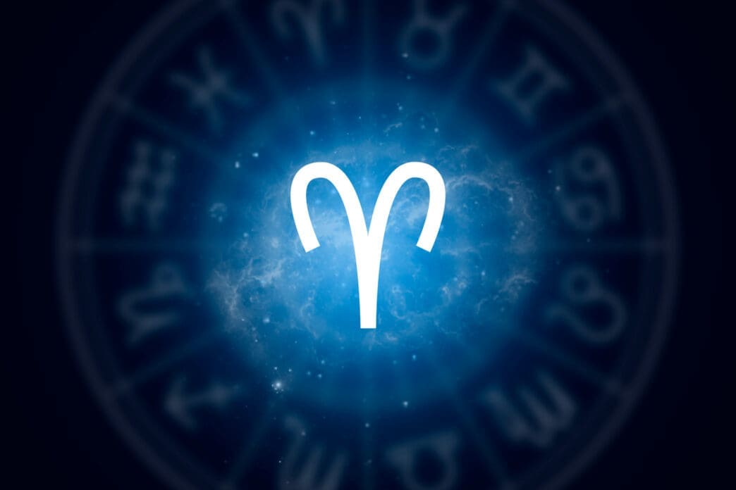 The bold white glyph for the Aries zodiac sign centered against a glowing blue nebula with a faint wheel of other signs