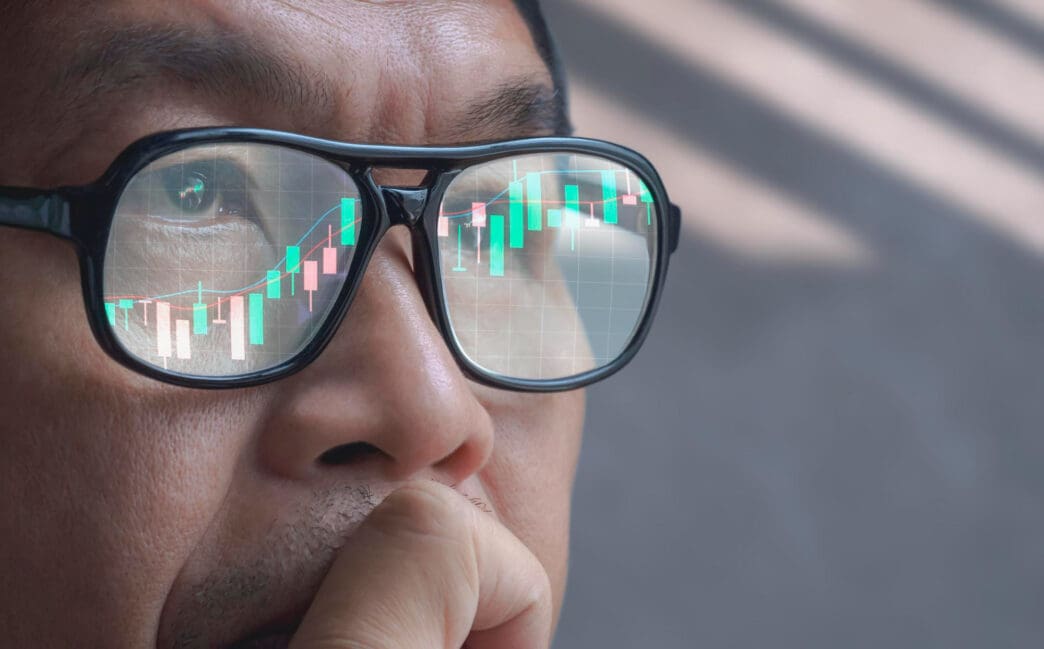 Close-up of an Asian trader's glasses reflecting a stock market candlestick chart.