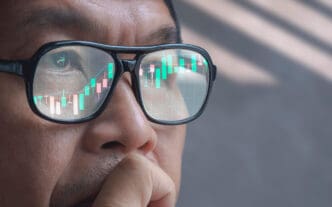 Close-up of an Asian trader's glasses reflecting a stock market candlestick chart.