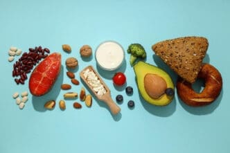 Flat lay of various high-protein, healthy fats, and whole grain foods, including salmon, beans, nuts, yogurt, and avocado, arranged on a blue background.