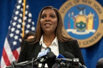 New York Attorney General Letitia James speaking at a podium filled with microphones, with the US and State seals behind her.