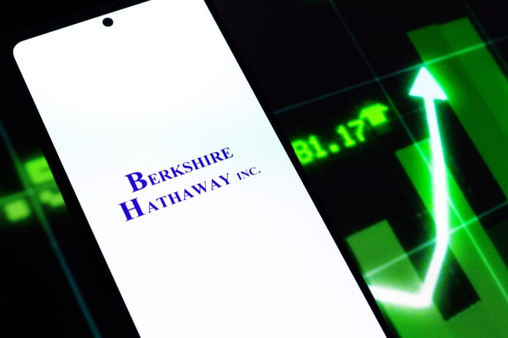 The Berkshire Hathaway logo on a smartphone screen, with a bullish stock chart in the background.