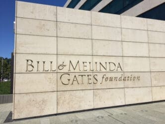 The name "Bill & Melinda Gates Foundation" carved into a large, segmented light-colored stone wall under bright sunlight.