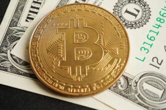 Close-up of a physical gold Bitcoin coin resting on top of a folded United States dollar bill.