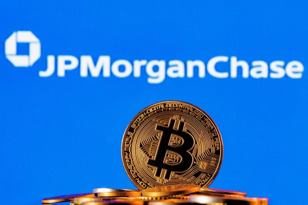 A golden Bitcoin coin on a pile of coins with the JPMorgan Chase logo in the background.