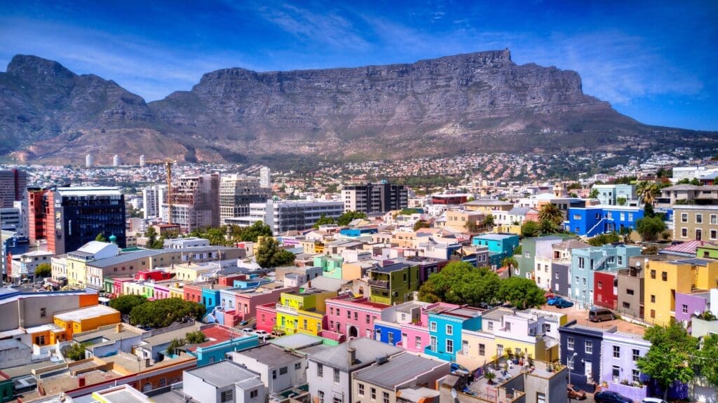 Panoramic view of the colorful Bo-Kaap neighborhood set against the massive, flat-topped Table Mountain in Cape Town, South Africa.