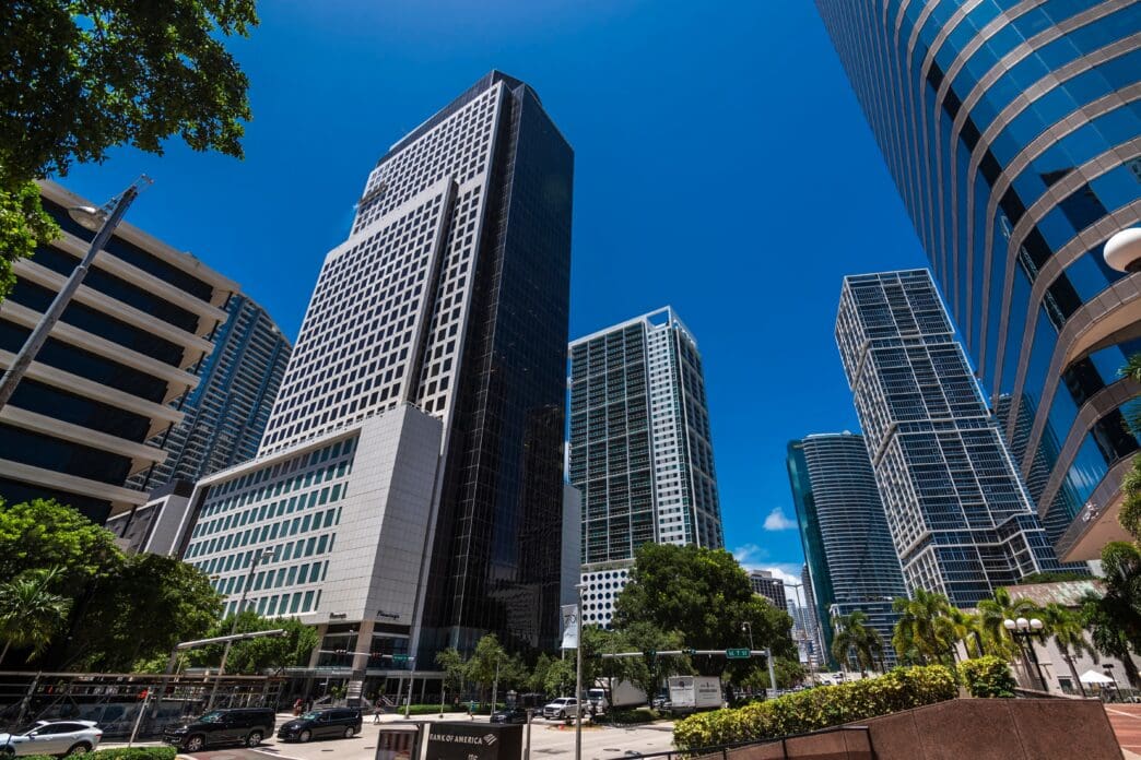 A street view of modern skyscrapers in Miami's Brickell financial district under a clear blue sky.