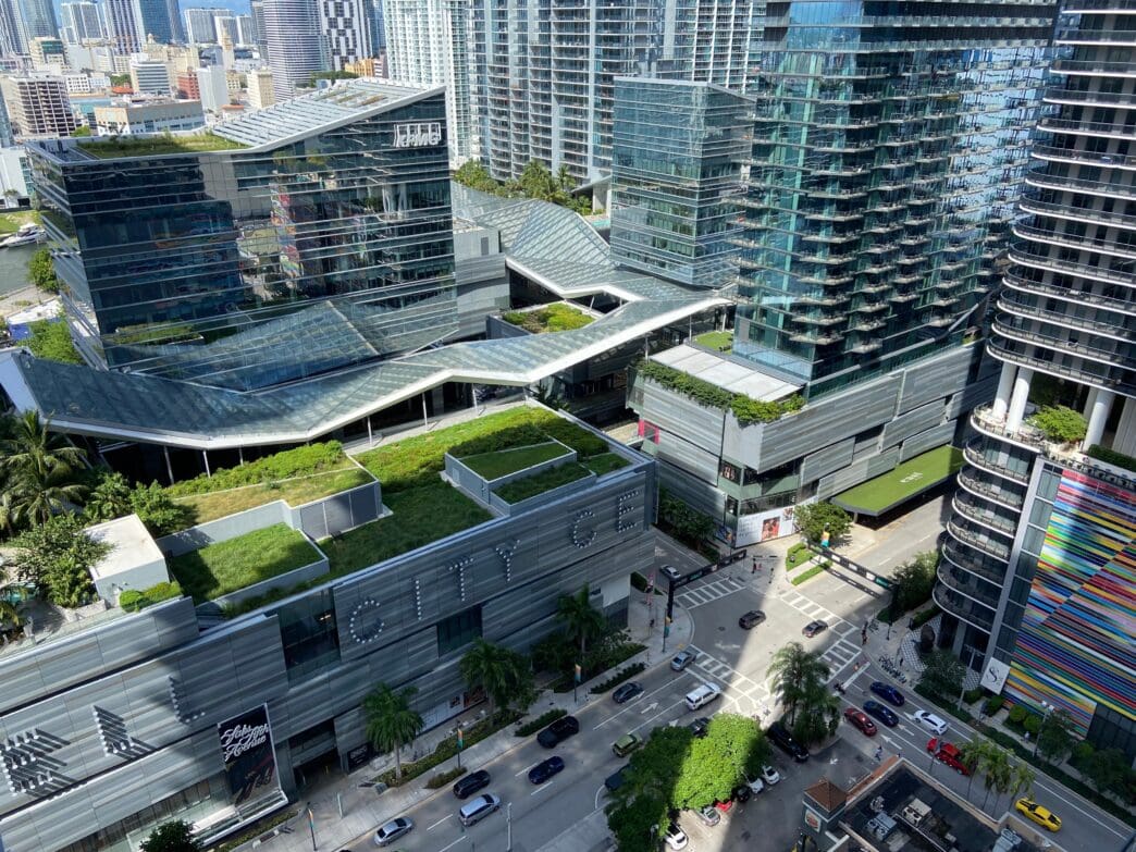 High aerial view of Brickell City Centre in Miami, showing its massive mixed-use complex with green roofs, surrounded by high-rise towers and street traffic.
