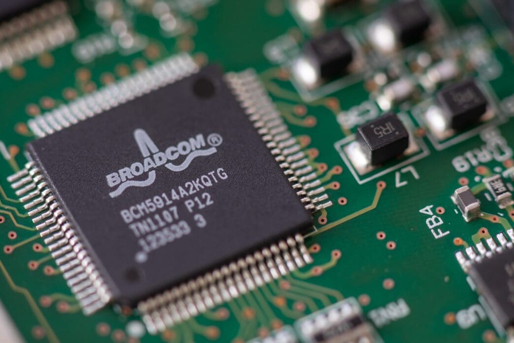A macro photograph of a black Broadcom ethernet controller microchip soldered onto a green printed circuit board.