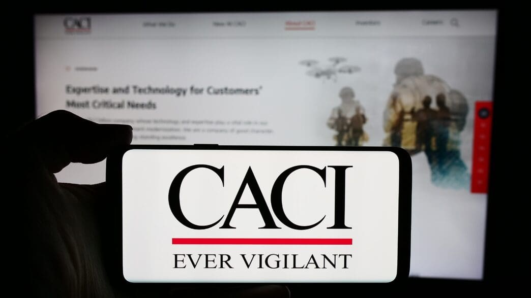 The CACI International Inc. logo on a smartphone screen, with the company's website in the background.