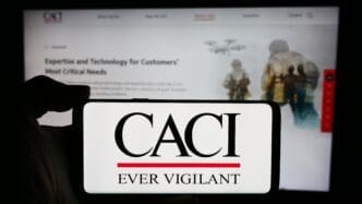The CACI International Inc. logo on a smartphone screen, with the company's website in the background.