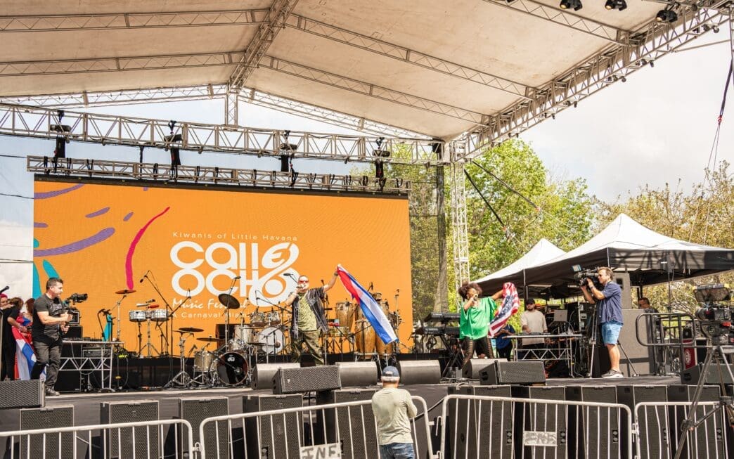 Performers on a large stage with a screen reading "Calle Ocho" at a festival.
