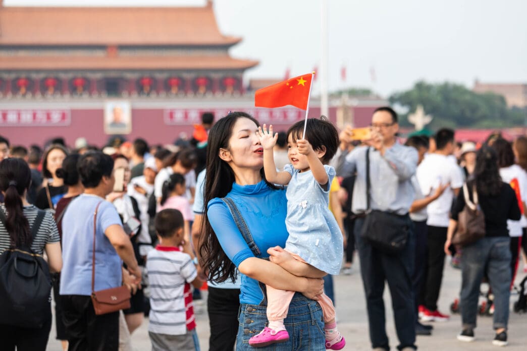 A mother holds her child aloft, waving a Chinese flag, amidst a crowd celebrating China's National Day in Tiananmen Square.
