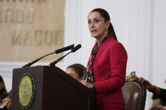Claudia Sheinbaum Pardo, Mexico City Mayor, speaking forcefully at a wooden podium with microphones during a formal presentation