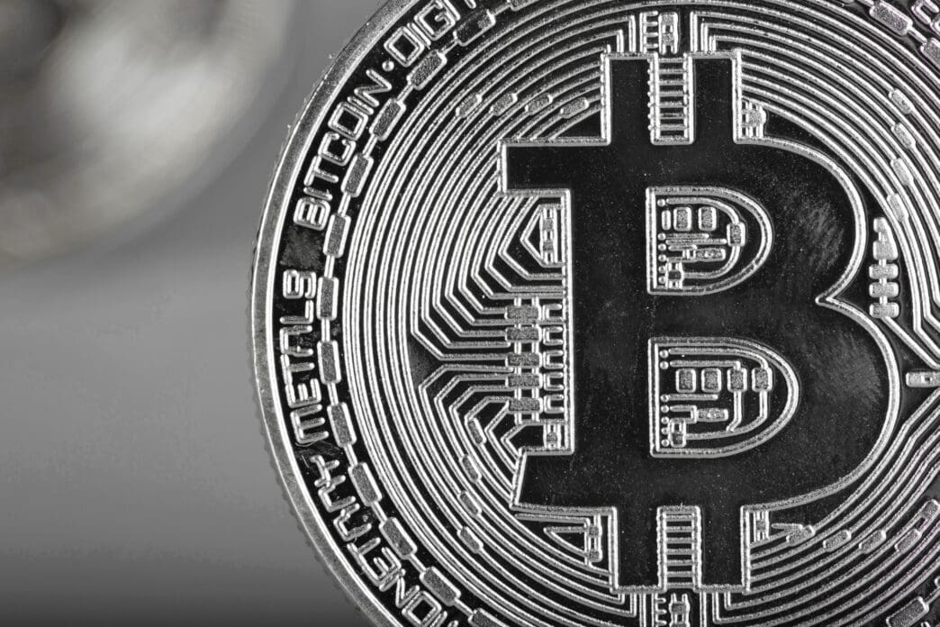 Extreme close-up of a physical silver Bitcoin coin showing the "B" symbol and intricate circuit-like engravings.