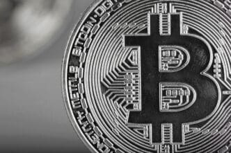 Extreme close-up of a physical silver Bitcoin coin showing the "B" symbol and intricate circuit-like engravings.