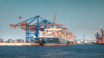 A large container ship docked at a busy port, being serviced by gantry cranes.
