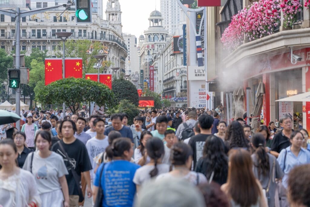 A massive crowd of pedestrians walking shoulder-to-shoulder on the historic Nanjing Road in Shanghai, decorated with Chinese flags.