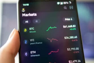 A smartphone screen displays a cryptocurrency market app, showing the prices and charts for Bitcoin, yearn.finance, and Ethereum.