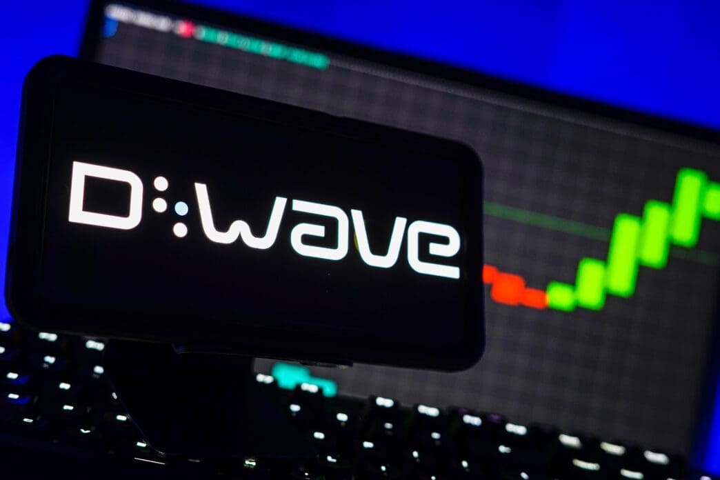 The D-Wave quantum computing logo is displayed on a smartphone, with a rising green stock market chart visible in the background.