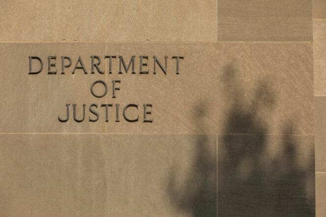 The "Department of Justice" sign is carved into the stone facade of the building in Washington, DC, with a shadow on the right.