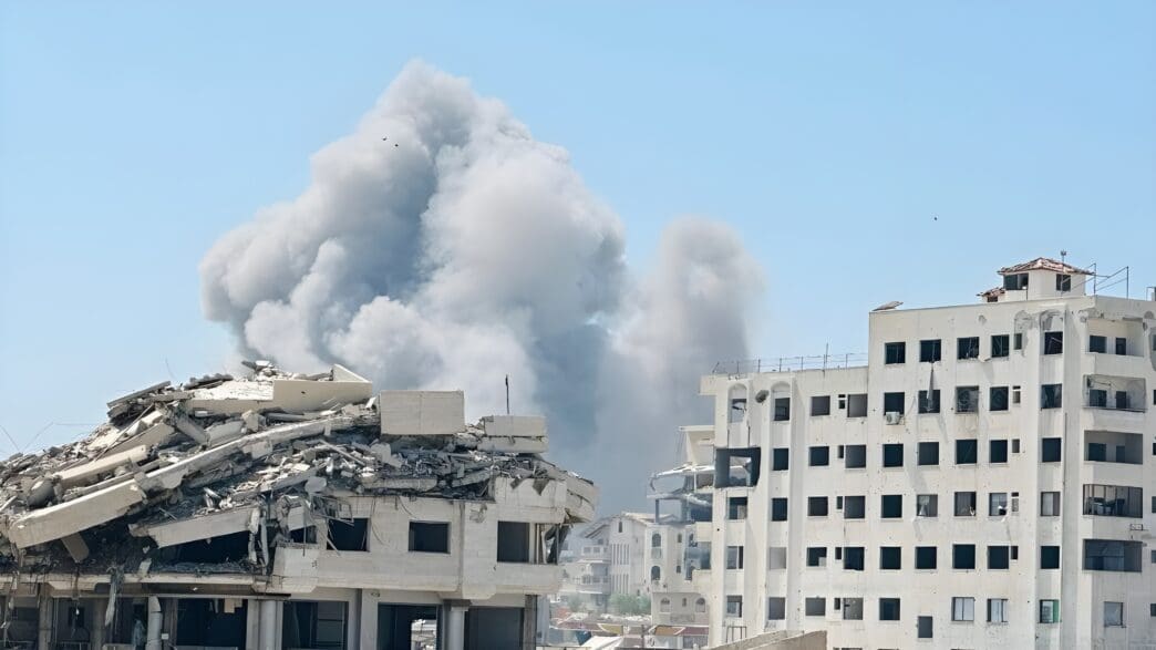 Damaged buildings with thick smoke rising into a clear blue sky