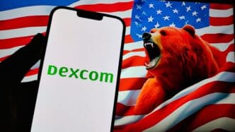 A phone displays the DexCom logo against a backdrop of a snarling red bear and the American flag, symbolizing a stock decline.