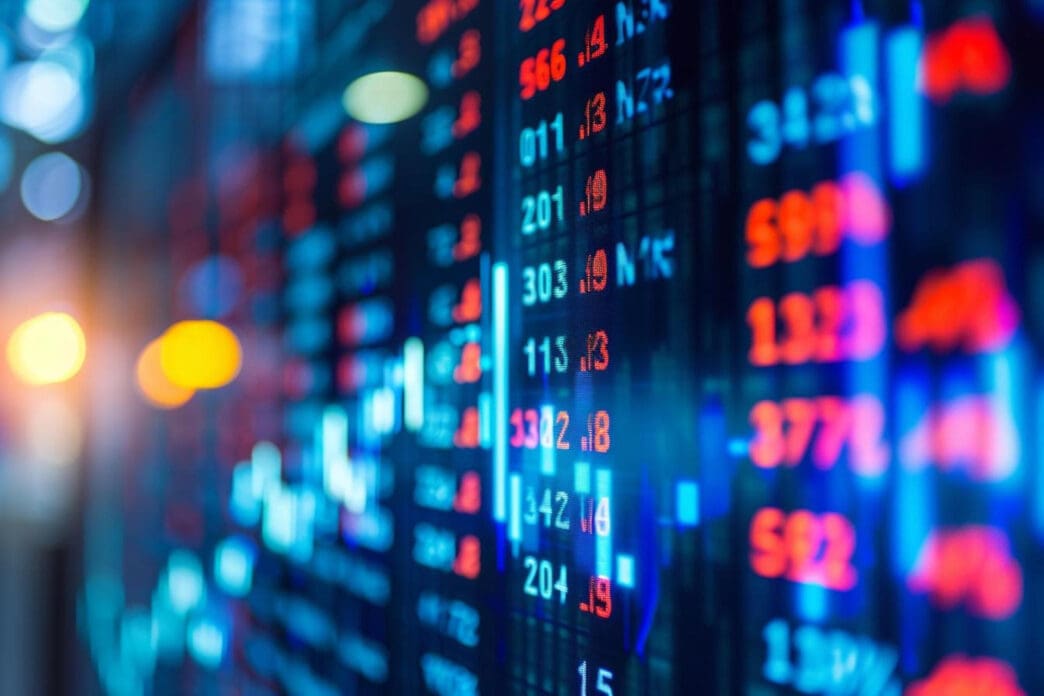 A close-up, angled shot of a digital stock market board, showing glowing red and blue financial data with a bokeh effect.