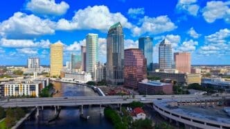 Aerial view of the downtown Tampa skyline featuring skyscrapers along the Hillsborough River under a bright, cloudy sky.