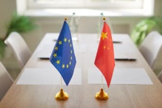 Small flags of the European Union and China on a wooden negotiation table.